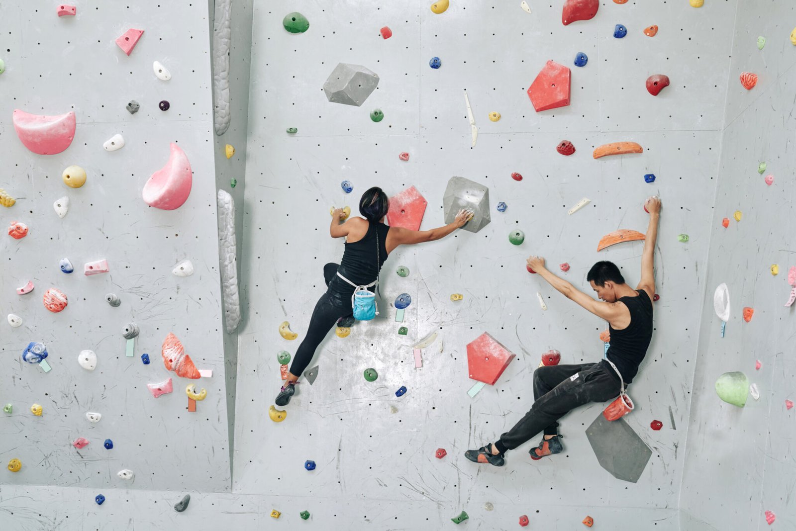 Strong young couple training in bouldering facility, they are climbing on artificial wall indoors